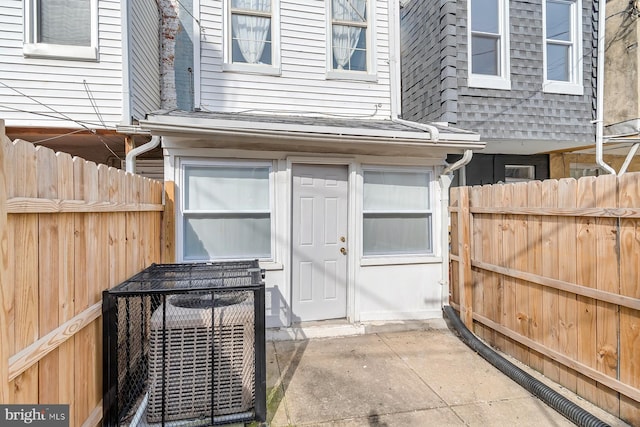 view of exterior entry with central air condition unit, a patio area, fence, and roof with shingles