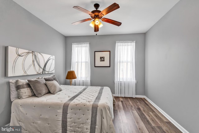 bedroom featuring a ceiling fan, multiple windows, baseboards, and wood finished floors