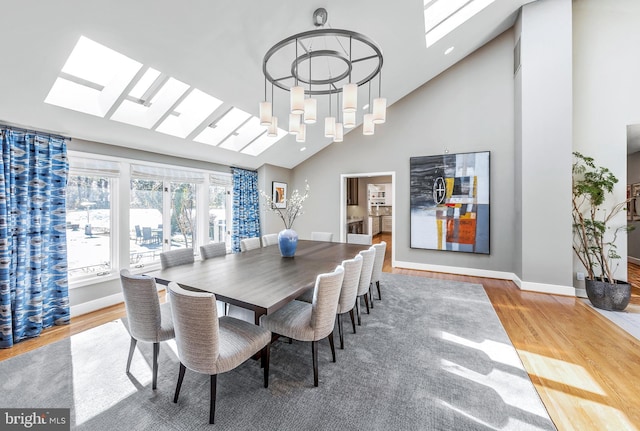 dining area with high vaulted ceiling, a skylight, wood finished floors, and baseboards