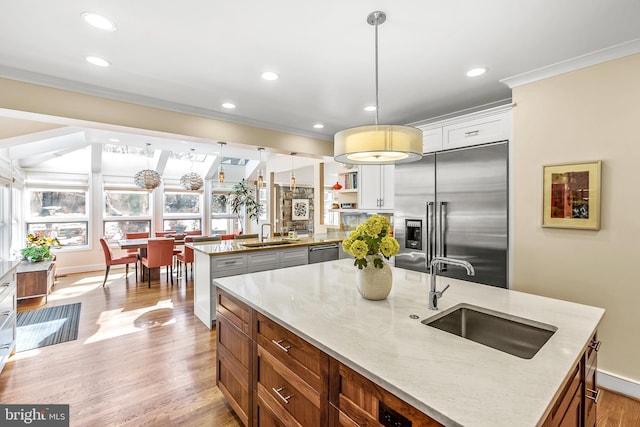 kitchen featuring crown molding, a center island with sink, stainless steel appliances, light wood-style floors, and a sink