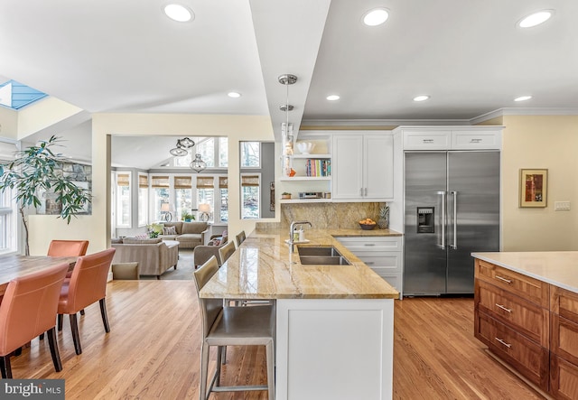 kitchen with a breakfast bar area, open shelves, white cabinetry, a sink, and built in refrigerator