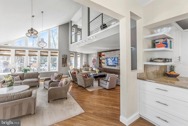 living room featuring baseboards, built in features, a towering ceiling, an inviting chandelier, and light wood-type flooring