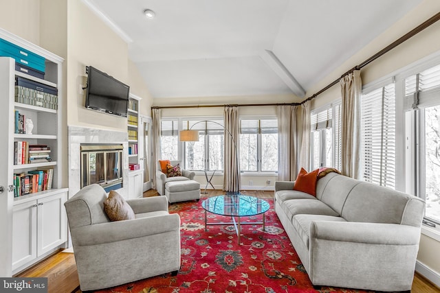 living area featuring lofted ceiling, light wood finished floors, baseboards, and a high end fireplace