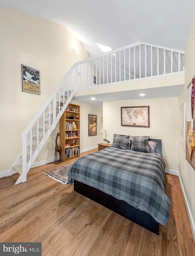 bedroom with high vaulted ceiling, baseboards, and wood finished floors