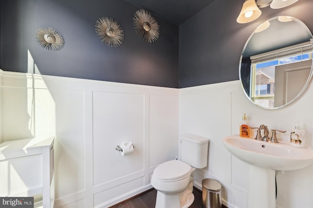 half bath with wainscoting, wood finished floors, toilet, and a decorative wall