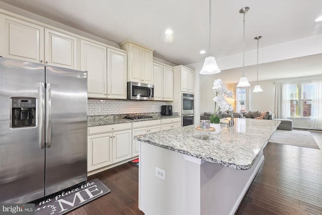 kitchen featuring tasteful backsplash, an island with sink, appliances with stainless steel finishes, light stone counters, and dark wood-style flooring