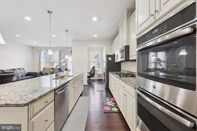 kitchen featuring dark wood-style floors, backsplash, appliances with stainless steel finishes, a sink, and an island with sink