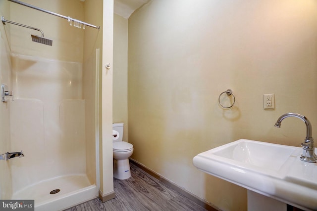 bathroom with toilet, wood finished floors, a sink, baseboards, and a stall shower