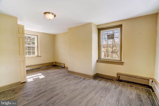 empty room with a healthy amount of sunlight, baseboard heating, and wood finished floors