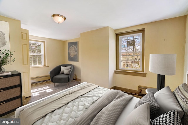 bedroom featuring a baseboard heating unit, wood finished floors, and baseboards