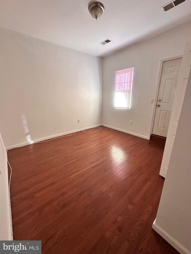 spare room with dark wood-type flooring, visible vents, and baseboards