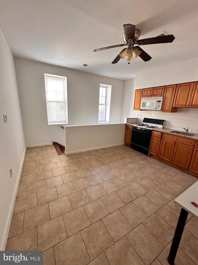 kitchen featuring white microwave, brown cabinets, backsplash, a sink, and gas stove