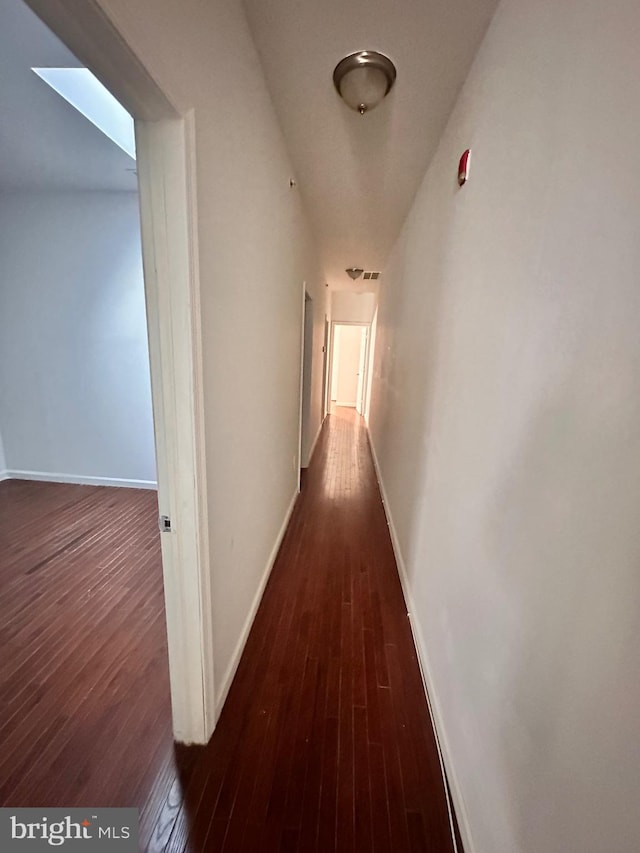 hallway with a skylight, baseboards, and hardwood / wood-style floors