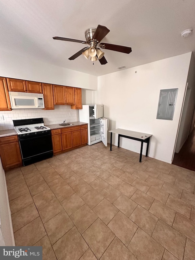 kitchen featuring gas range oven, backsplash, white microwave, brown cabinetry, and electric panel