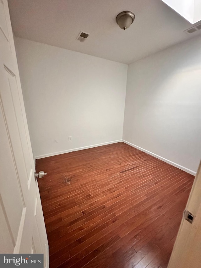 empty room with baseboards, visible vents, and wood finished floors