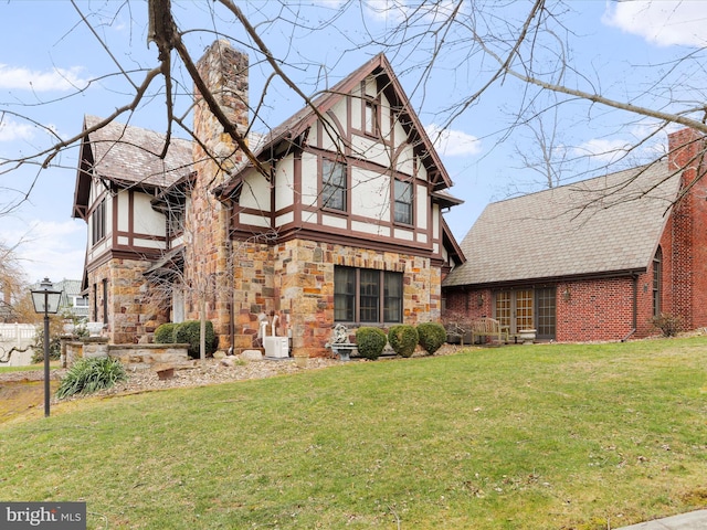 tudor home with stucco siding, stone siding, a chimney, and a front yard