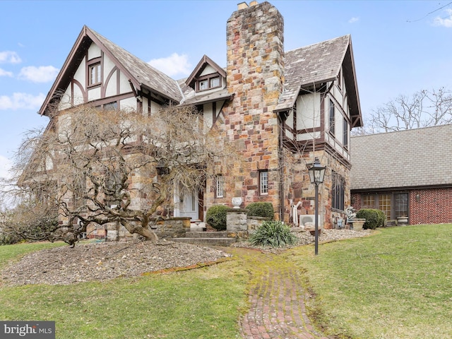 tudor house featuring a front yard, stone siding, and a chimney