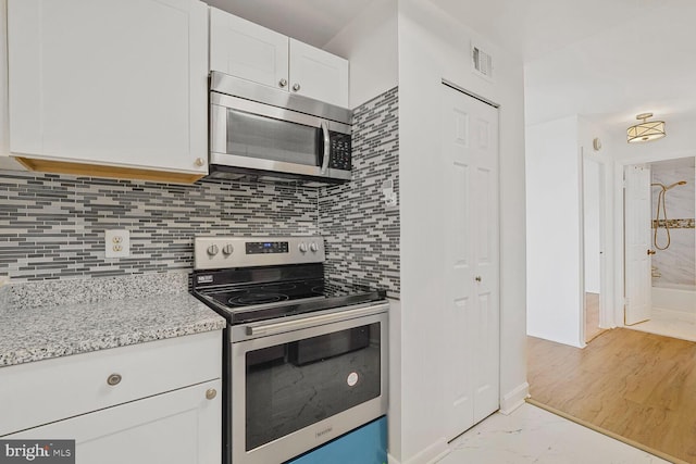 kitchen featuring light stone counters, visible vents, appliances with stainless steel finishes, white cabinetry, and backsplash