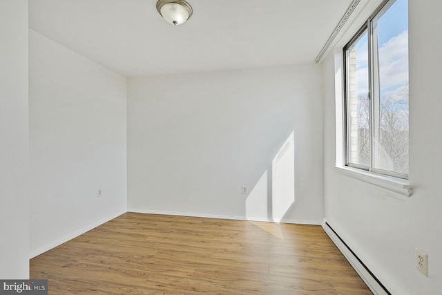 spare room with a baseboard heating unit, wood finished floors, and baseboards