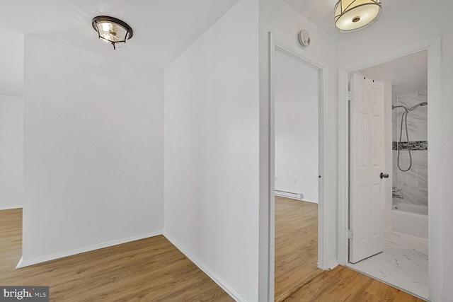 corridor featuring baseboards, baseboard heating, and wood finished floors