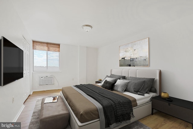 bedroom with a wall mounted air conditioner, baseboards, and wood finished floors