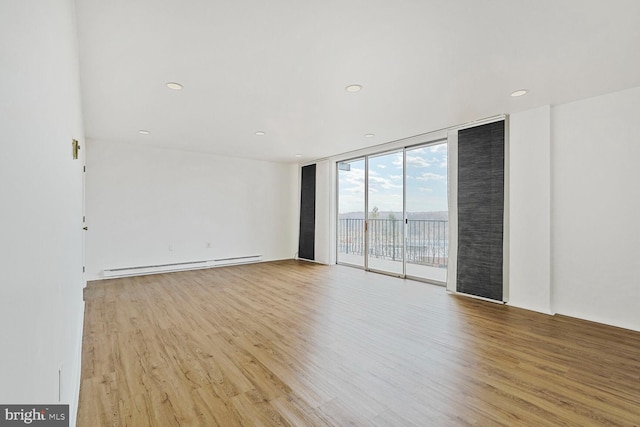 unfurnished room with a wall of windows, a baseboard radiator, light wood-type flooring, and recessed lighting