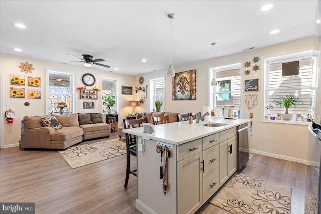 kitchen with a sink, an island with sink, light wood-type flooring, dishwasher, and a kitchen breakfast bar