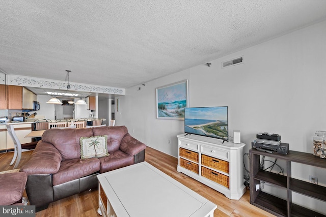 living area featuring visible vents, light wood-style flooring, and a textured ceiling