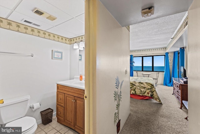 ensuite bathroom with visible vents, vanity, toilet, and a textured ceiling