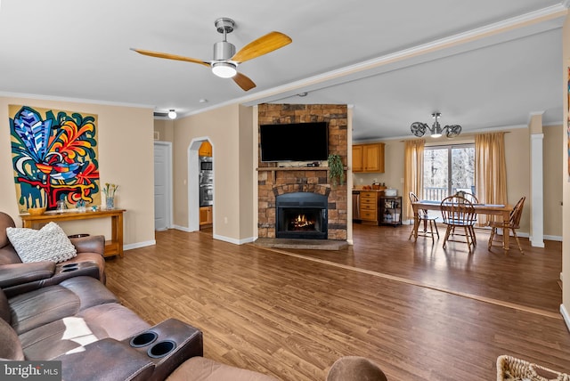 living room featuring arched walkways, ornamental molding, a stone fireplace, light wood-type flooring, and baseboards