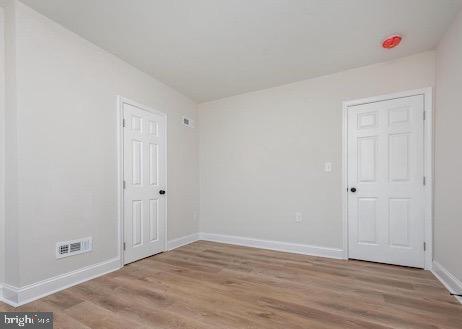 empty room with light wood-style floors, baseboards, and visible vents