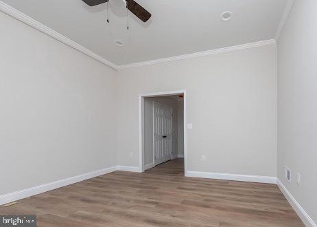 spare room with a ceiling fan, crown molding, baseboards, and wood finished floors