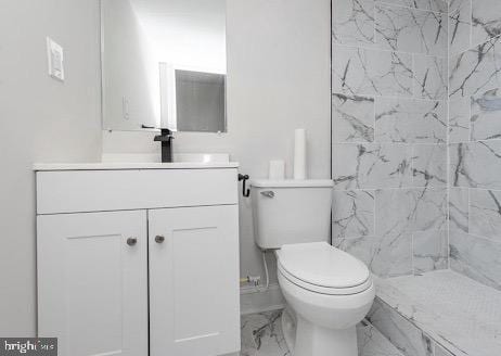 bathroom with marble finish floor, a tile shower, vanity, and toilet