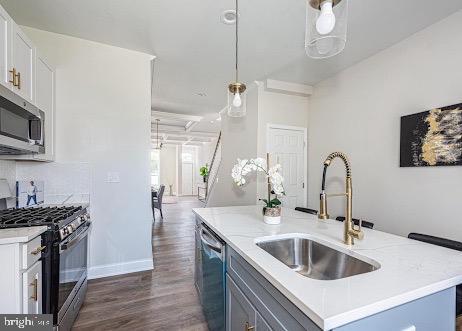 kitchen featuring dark wood-style flooring, stainless steel appliances, hanging light fixtures, a kitchen island with sink, and a sink