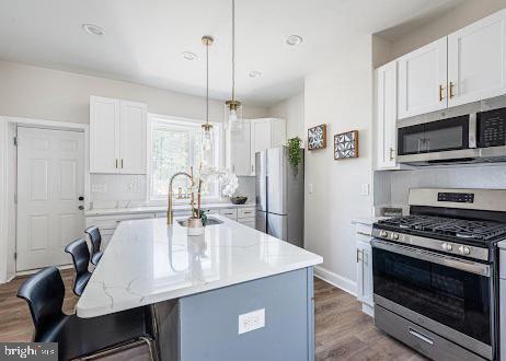 kitchen featuring stainless steel appliances, wood finished floors, a sink, a kitchen breakfast bar, and decorative light fixtures