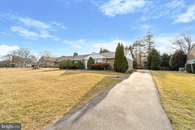 view of front of property featuring a front yard, stone siding, fence, and a residential view