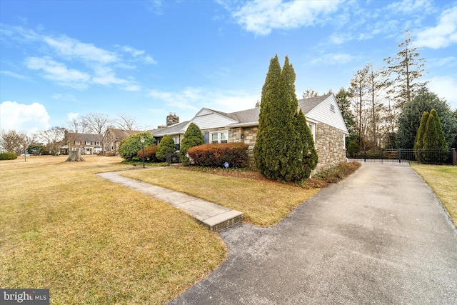 view of property exterior featuring stone siding, a lawn, and fence