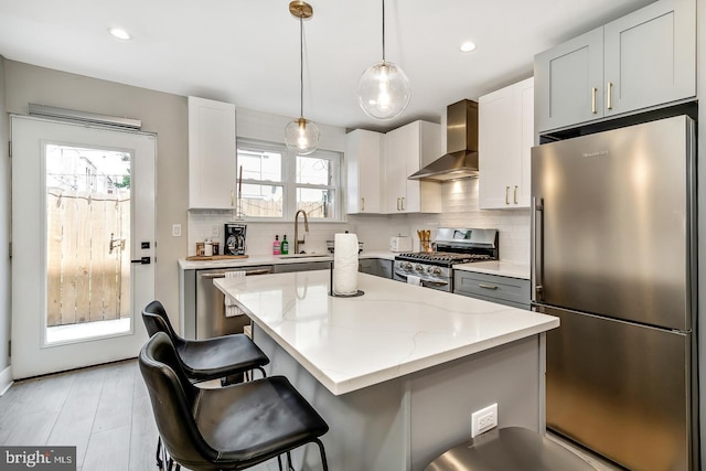 kitchen featuring decorative backsplash, appliances with stainless steel finishes, a sink, wall chimney range hood, and a kitchen bar