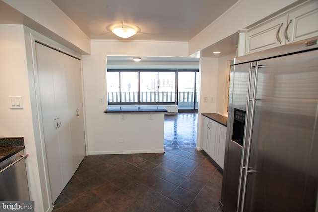 kitchen with dark countertops, white cabinetry, high quality fridge, and baseboards