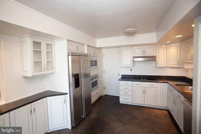 kitchen with under cabinet range hood, glass insert cabinets, dark countertops, and appliances with stainless steel finishes