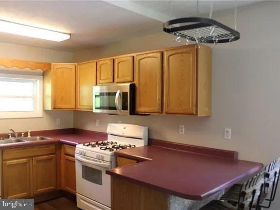 kitchen with a peninsula, a sink, a kitchen breakfast bar, white gas range oven, and stainless steel microwave