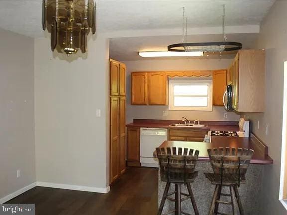 kitchen with baseboards, dark wood finished floors, dishwasher, stainless steel microwave, and a sink