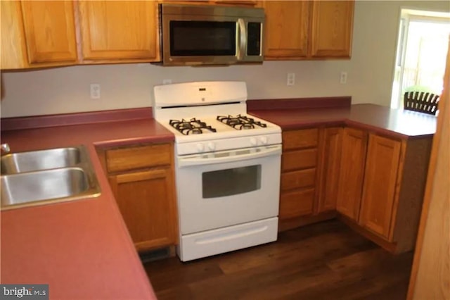 kitchen with stainless steel microwave, a peninsula, dark wood-style flooring, a sink, and gas range gas stove