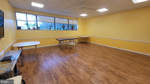 recreation room featuring a ceiling fan, wood finished floors, baseboards, and a drop ceiling