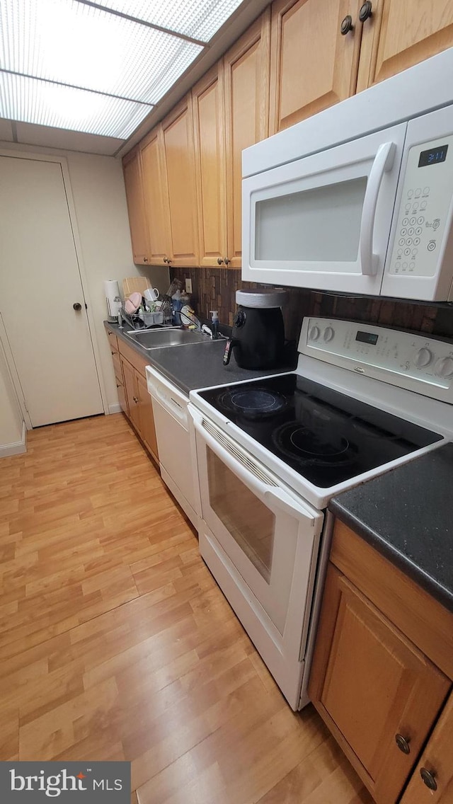 kitchen featuring white appliances, light wood-style flooring, dark countertops, and a sink