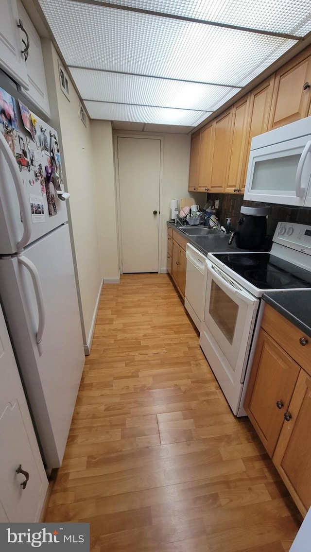 kitchen with dark countertops, visible vents, light wood-style floors, white appliances, and a sink