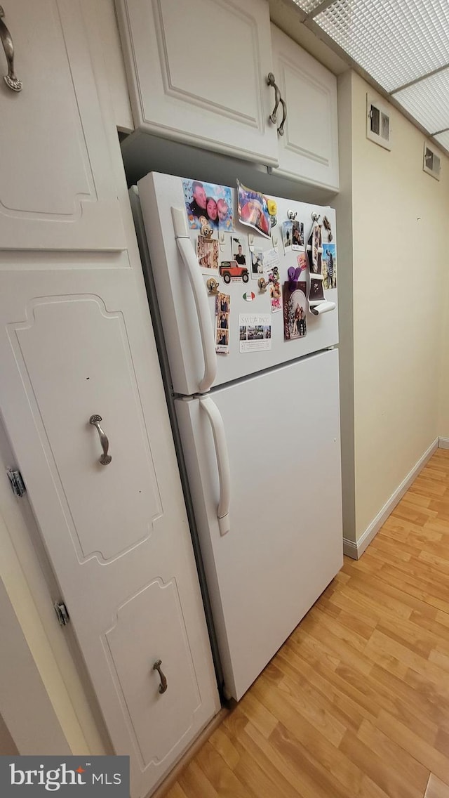 kitchen featuring visible vents, white cabinetry, freestanding refrigerator, light wood-style floors, and baseboards