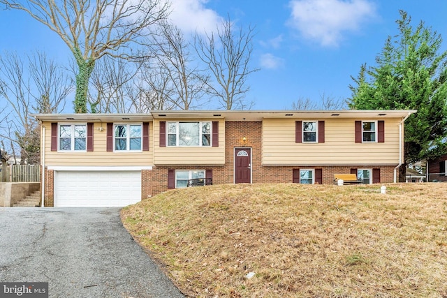 split foyer home with a front yard, an attached garage, brick siding, and driveway