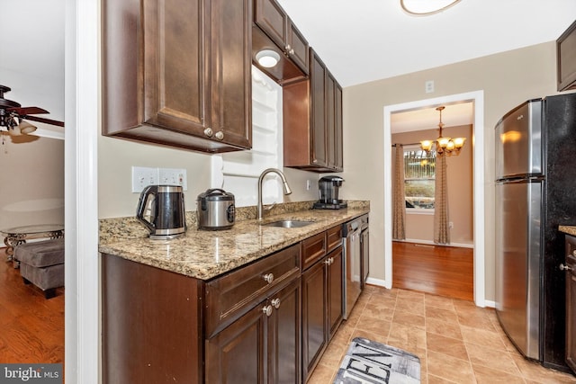 kitchen featuring dark brown cabinets, light stone counters, ceiling fan with notable chandelier, appliances with stainless steel finishes, and a sink