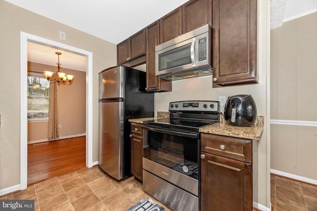 kitchen featuring a notable chandelier, dark brown cabinetry, appliances with stainless steel finishes, baseboards, and light stone countertops